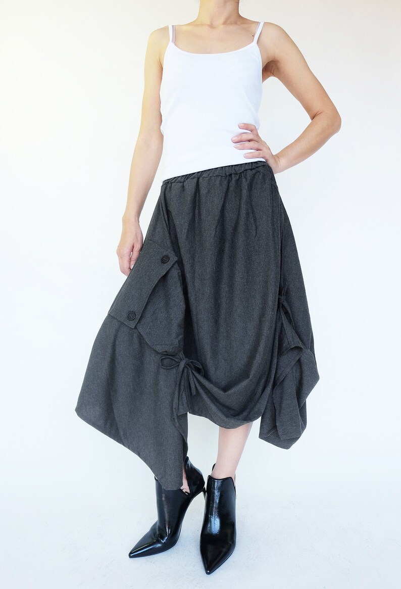 May include: A gray asymmetrical skirt with a large pocket on the side and a bow detail. The skirt is made of a soft, drapey fabric and has a relaxed fit.