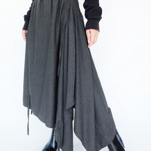 May include: A charcoal gray asymmetrical skirt with a drawstring waist and long ties. The skirt is made of a soft, drapey fabric and has a flowing silhouette.