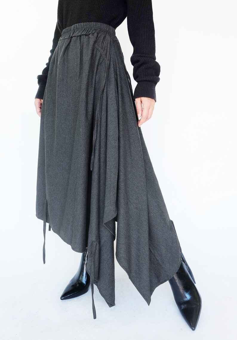 May include: A charcoal gray asymmetrical skirt with a drawstring waist and long ties. The skirt is made of a soft, drapey fabric and has a flowing silhouette.