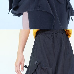 May include: Black skirt with a unique design featuring a large pocket on the side and a tie detail at the bottom. The skirt has a drawstring waist and a relaxed fit.