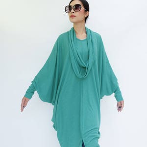 K&ouml;nnte beinhalten: Ein t&uuml;rkisfarbenes Tunika mit Wasserfallausschnitt und Fledermaus&auml;rmeln. Das lang&auml;rmlige Oberteil wird mit einer dunkelblauen Jeans kombiniert. Das Model tr&auml;gt eine gro&szlig;e, dunkle Sonnenbrille.
