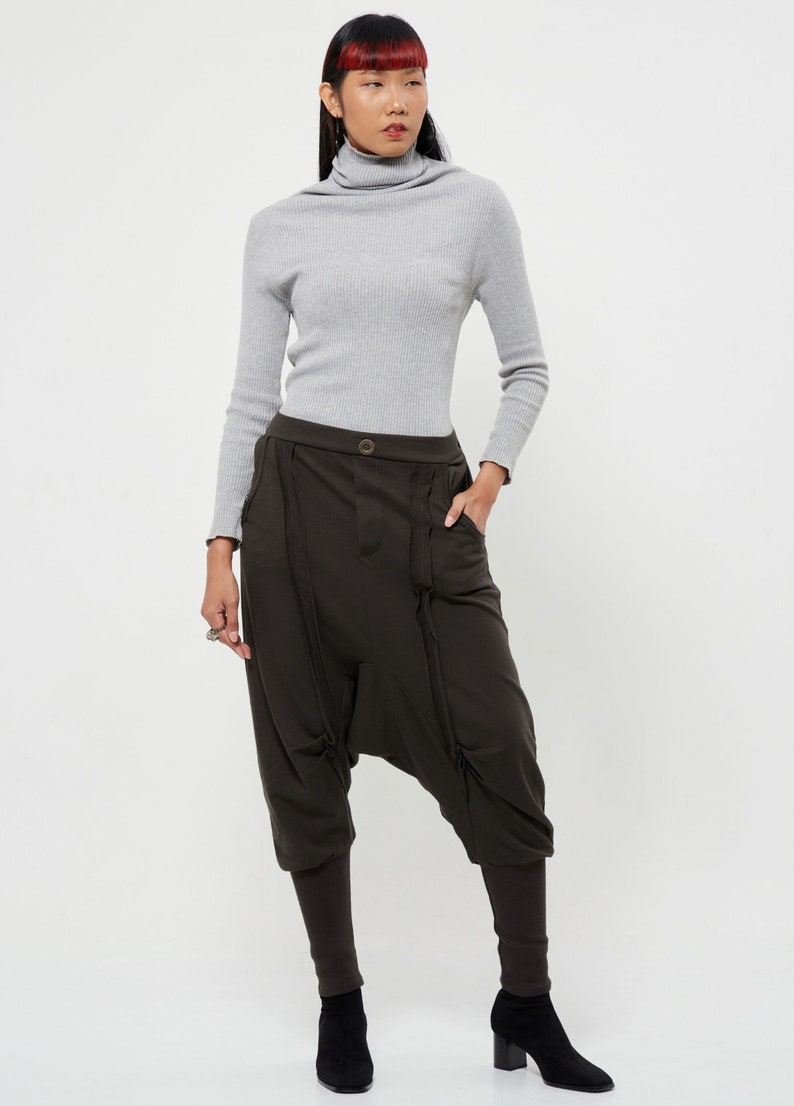 May include: A woman is wearing a gray turtleneck sweater and brown, loose-fitting pants with a unique design. The pants have a wide leg and a gathered detail at the ankles.