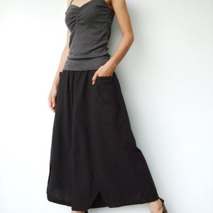 May include: A woman wearing a gray tank top and a long black skirt with a side slit. She is wearing black sandals with cork wedges.