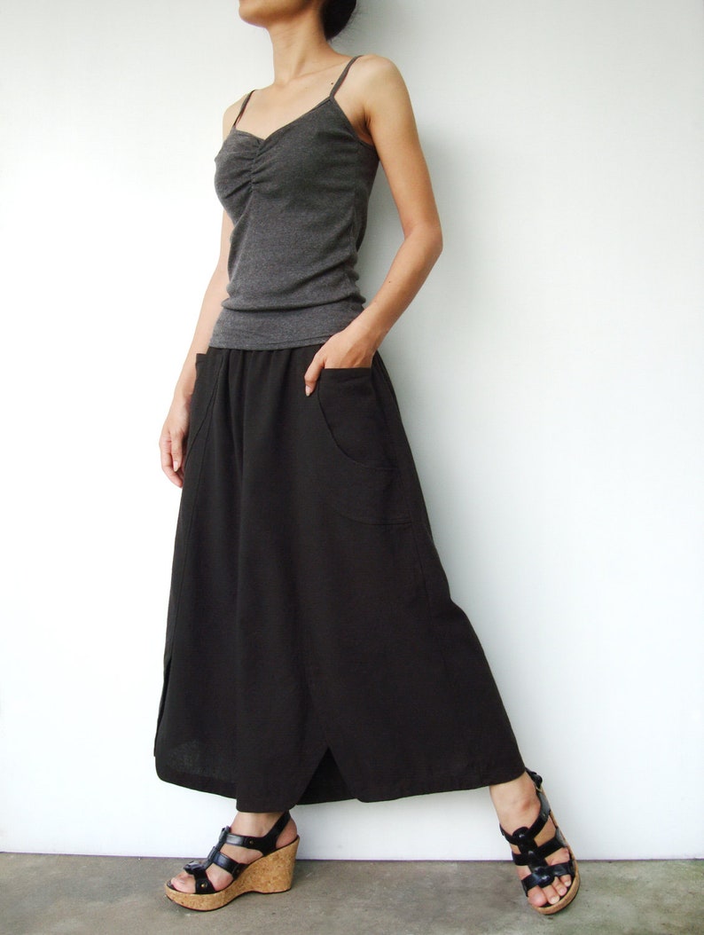 May include: A woman wearing a gray tank top and a long black skirt with a side slit. She is wearing black sandals with cork wedges.