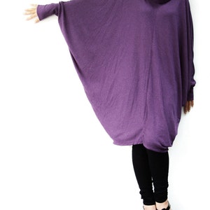 Puede incluir: Una t&uacute;nica larga y holgada de color morado con cuello de tortuga y mangas largas. La t&uacute;nica est&aacute; hecha de una tela suave y fluida y se lleva con leggings negros y sandalias negras.