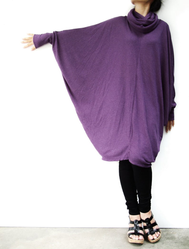 Puede incluir: Una t&uacute;nica larga y holgada de color morado con cuello de tortuga y mangas largas. La t&uacute;nica est&aacute; hecha de una tela suave y fluida y se lleva con leggings negros y sandalias negras.