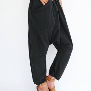 Pu&ograve; includere: Pantaloni in cotone nero con una vestibilit&agrave; ampia e larga, con una cintura elastica larga. I pantaloni hanno un design unico con pi&ugrave; cuciture e una grande tasca sul davanti.