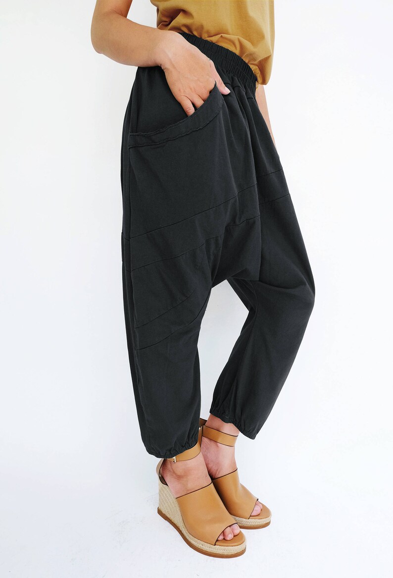 Pu&ograve; includere: Pantaloni in cotone nero con una vestibilit&agrave; ampia e larga, con una cintura elastica larga. I pantaloni hanno un design unico con pi&ugrave; cuciture e una grande tasca sul davanti.