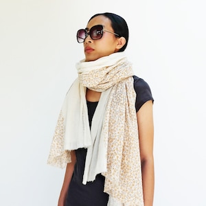 May include: A woman wearing a white and beige floral patterned scarf with a black t-shirt and sunglasses.
