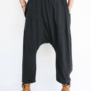 Pu&ograve; includere: Pantaloni in cotone nero con una vestibilit&agrave; ampia e larga e una cintura con coulisse. I pantaloni hanno un design unico con cuciture diagonali e un cavallo basso.