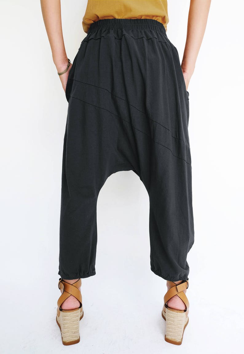 Pu&ograve; includere: Pantaloni in cotone nero con una vestibilit&agrave; ampia e larga e una cintura con coulisse. I pantaloni hanno un design unico con cuciture diagonali e un cavallo basso.
