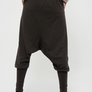 May include: Dark brown, loose-fitting pants with a wide, gathered leg. The pants have a drawstring waistband and a relaxed fit.