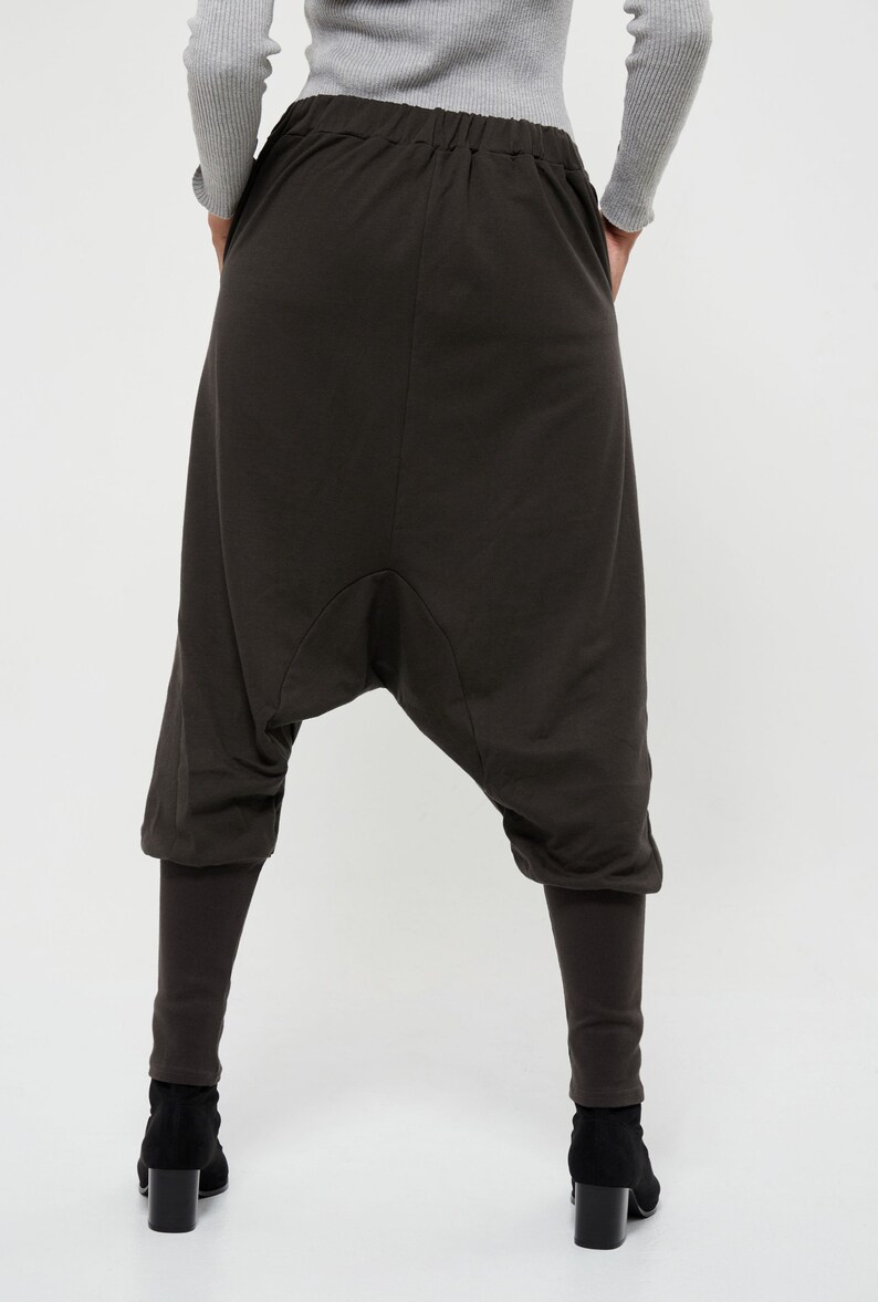 May include: Dark brown, loose-fitting pants with a wide, gathered leg. The pants have a drawstring waistband and a relaxed fit.