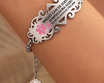May include: A silver-toned medical alert bracelet featuring an ornate, filigree-style rectangular plate. The plate is engraved with the text BREAST CANCER SURVIVOR, LYMPHEDEMA ALERT, NO BP/IV/NEEDLES THIS ARM, and a pink ribbon with a medical star.