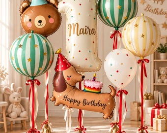 Puede incluir: Un conjunto de globos de cumpleaños que incluye un oso marrón con un gorro de fiesta azul, un globo con el número uno en color crema con el nombre Maira, un perro salchicha con un pastel y varios globos redondos a rayas y lunares en verde, oro y blanco.