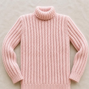 Könnte beinhalten: Ein hellrosa Langarmpullover mit einer ausgeprägten Rippstrickstruktur am gesamten Körper und an den Ärmeln. Das Kleidungsstück verfügt über einen hohen, umgeschlagenen Rollkragen, gerippte Bündchen an den Ärmeln und einen gerippten Saum.
