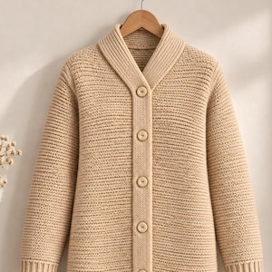 May include: A beige long-sleeve cardigan featuring a thick ribbed knit texture, a shawl collar, and a front button closure with six matching round buttons. The garment has ribbed cuffs and a straight hem, constructed from a solid light tan yarn.