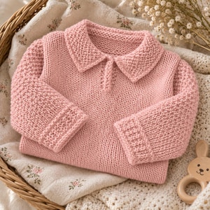 Könnte beinhalten: Ein langärmeliger, hellrosa Strickpullover mit einem Kragen und einem strukturierten Perlmuster an Kragen und Ärmelbündchen. Der Hauptteil des Pullovers ist in glattem Rechtsstrick gefertigt, was für ein gleichmäßiges und weiches Erscheinungsbild sorgt.