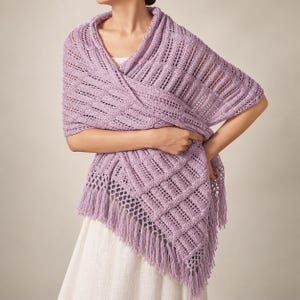 May include: A lavender knit shawl featuring a textured pattern of vertical columns and horizontal bands. The garment is draped over the shoulders and includes a fringe trim along the bottom edge, creating a layered appearance with openwork details.