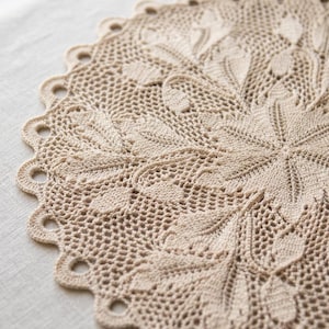 Könnte beinhalten: Ein rundes, beiges Häkeldeckchen mit einem komplizierten Blumen- und Blattmuster und einem gewellten Rand. Die Textilarbeit zeigt ein detailliertes Durchbruchdesign mit miteinander verbundenen Maschen, die ein zentrales Motiv bilden.