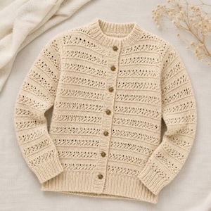 Könnte beinhalten: Eine cremefarbene Strickjacke mit langen Ärmeln, Rundhalsausschnitt, gerippten Bündchen und einer vertikalen Knopfleiste. Das Kleidungsstück zeigt ein wiederkehrendes Muster aus horizontalen Lochmusterstreifen, die sich mit glatten Strickpartien abwechseln.