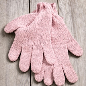 May include: A pair of soft, light pink knitted gloves featuring a classic five-finger design with ribbed cuffs. The knit texture is consistent throughout, showcasing a simple, functional construction with a uniform pastel color and a visible weave.