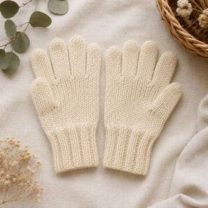 May include: A pair of cream-colored knit gloves featuring a classic stockinette stitch pattern on the hand and a ribbed cuff at the wrist. The gloves are constructed with five fingers and have a consistent, uniform texture throughout the design.