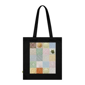 May include: A black tote bag featuring a central rectangular graphic composed of a grid of twenty square tiles. Each tile displays a unique embossed pattern in pastel shades, including a sun, a sea turtle, and various floral and geometric motifs.