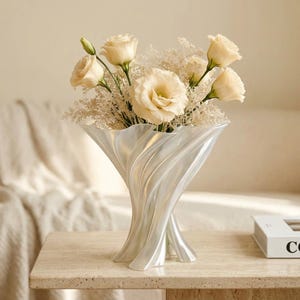 May include: A pearlescent white vase with a flared, rippled, and sculptural design. The vase contains a bouquet of cream-coloured eustoma flowers and delicate, feathery white filler foliage, creating a soft and elegant floral arrangement.