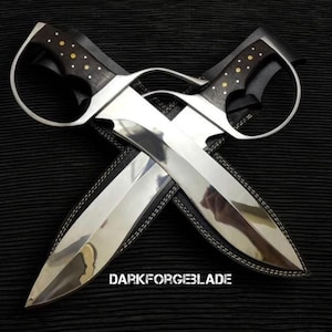 May include: Two crossed knives with polished silver blades and dark wooden handles featuring gold-colored rivets and circular metal guards. The text DARKFORGEBLADE is printed in white at the bottom center. The knives are resting on black sheaths.
