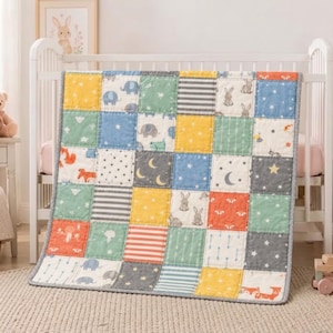 Puede incluir: Una colcha de patchwork que presenta una cuadrícula de paneles de tela cuadrados en amarillo, azul, verde, naranja y gris. La colcha muestra varios patrones que incluyen elefantes, conejos, zorros, estrellas, lunas, rayas y flechas.