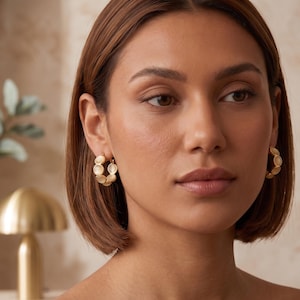 May include: A pair of gold hoop earrings featuring a series of small, circular, translucent white stone accents arranged along the outer edge of each hoop. The earrings have a polished gold metal finish and a secure clasp mechanism for attachment.