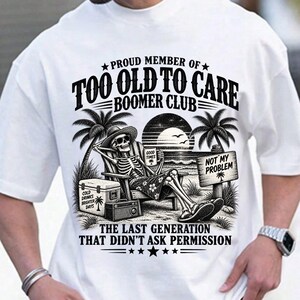 May include: A white t-shirt featuring a black graphic of a skeleton sitting in a beach chair under palm trees. The text reads: PROUD MEMBER OF TOO OLD TO CARE BOOMER CLUB, GOOD TIMES, NOT MY PROBLEM, COLD DRINKS BRIGHTER DAYS, THE LAST GENERATION THAT DIDN'T ASK PERMISSION.
