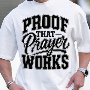May include: A white short-sleeved t-shirt featuring bold black text on the front that reads PROOF THAT Prayer WORKS. The word PROOF and WORKS are in a large block font, while the word Prayer is in a stylized, cursive script font.