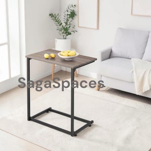 May include: A C-shaped side table with a dark wood grain rectangular top and a black metal frame. The table features a sturdy base designed to slide under furniture. The text SagaSpaces is overlaid on the image in a dark gray font.