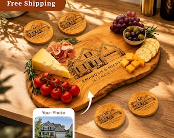 May include: A live-edge wooden serving board engraved with a house illustration and the text AMANDAH & MICHAEL 1520 MAIN ST. CA, accompanied by four matching round wooden coasters, a wedge of cheese, cherry tomatoes, grapes, and olives.