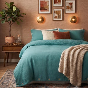 May include: A teal duvet cover with visible button closures along the edges, paired with matching teal pillowcases, a cream textured throw blanket, a rust-colored velvet pillow, and a cream decorative pillow on a bed against a textured wall.