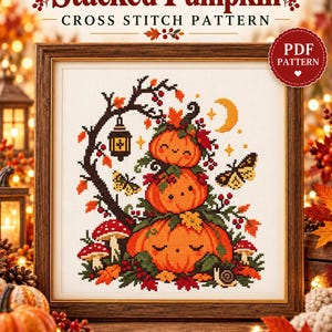 May include: A cross stitch pattern titled Stacked Pumpkin featuring three orange pumpkins with faces stacked vertically, surrounded by mushrooms, a lantern, butterflies, a snail, and autumn leaves, all framed in a dark wood frame.