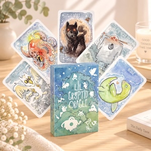 May include: A deck of Lil Cryptid Oracle cards featuring watercolor illustrations of mythical creatures including an octopus, a black wolf, a three-eyed figure, a bird-like creature, and a green sea monster, with a box labeled Lil Cryptid Oracle.