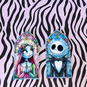 Peut inclure: Deux broches rectangulaires en émail avec des motifs de vitraux en arc. L'une représente un personnage féminin aux longs cheveux roses et à la robe colorée, l'autre un personnage masculin squelettique en costume rayé et nœud papillon.