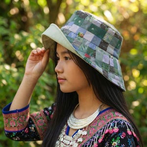 May include: A bucket hat featuring a patchwork design of various green, purple, and white fabric squares. The hat has a wide, solid light green brim and a structured crown. The patchwork pattern includes subtle floral and geometric prints.