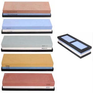 May include: A collection of rectangular sharpening stones in various colours including tan, light blue, grey, yellow, and red. Each stone is dual-sided with printed grit numbers such as 240, 800, 600, 1500, 1000, 4000, 5000, 2000, 3000, and 8000, set in black bases.