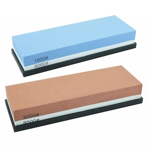 May include: Two rectangular sharpening stones, each featuring two distinct grit layers and a black base. The top stone is light blue and white with 1000# and 6000# markings. The bottom stone is terracotta and white with 3000# and 8000# markings.