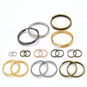 May include: A collection of metal split rings in various sizes and finishes, including silver, gold, bronze, gunmetal, and copper tones. These circular hardware components feature a double-loop coil design, arranged in multiple rows on a white surface.