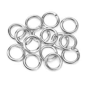 May include: A collection of small, circular silver-toned metal jump rings. Each ring features a single split opening, allowing for easy connection and assembly in jewellery making or craft projects. The rings have a smooth, polished metallic finish.