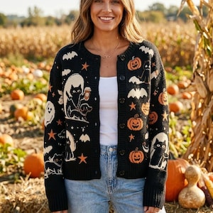 May include: A black button-down knit cardigan featuring a repeating Halloween-themed pattern of orange pumpkins, white ghosts, bats, stars, and black cats, some of which are depicted holding coffee cups, with a ribbed collar, cuffs, and hem.