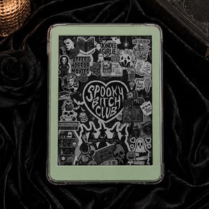 Peut inclure: Une housse de liseuse vert clair ornée d'un collage d'autocollants noirs et blancs sur le thème de l'horreur. L'autocollant central en forme de cœur porte l'inscription "SPOOKY BITCH CLUB" entourée d'illustrations de crânes, de fantômes et de personnages.