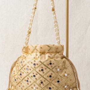 May include: A beige drawstring pouch bag featuring a gold lattice pattern with small circular mirrors embedded in each diamond section. The bag includes a long handle made of white pearl beads and gold accents, with gold bell-shaped tassels.