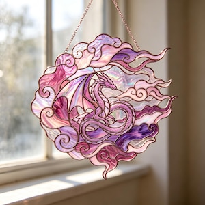 May include: A circular stained glass suncatcher featuring a dragon surrounded by swirling clouds in shades of iridescent pink and purple. The piece is constructed with copper-toned metal cames and hangs from a matching delicate metal chain.
