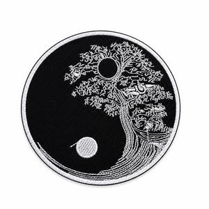 May include: A circular embroidered patch featuring a black and white design that mimics the yin and yang symbol. The imagery depicts a detailed tree with white stitching on a black background, incorporating a circular sun and moon motif.